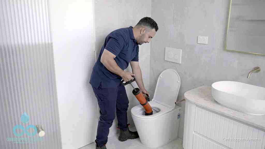 Een monteur buigt over een wandcloset en duwt met de hand een persluchtontstopper in de toiletpot om de verstopping handmatig los te maken in Almere