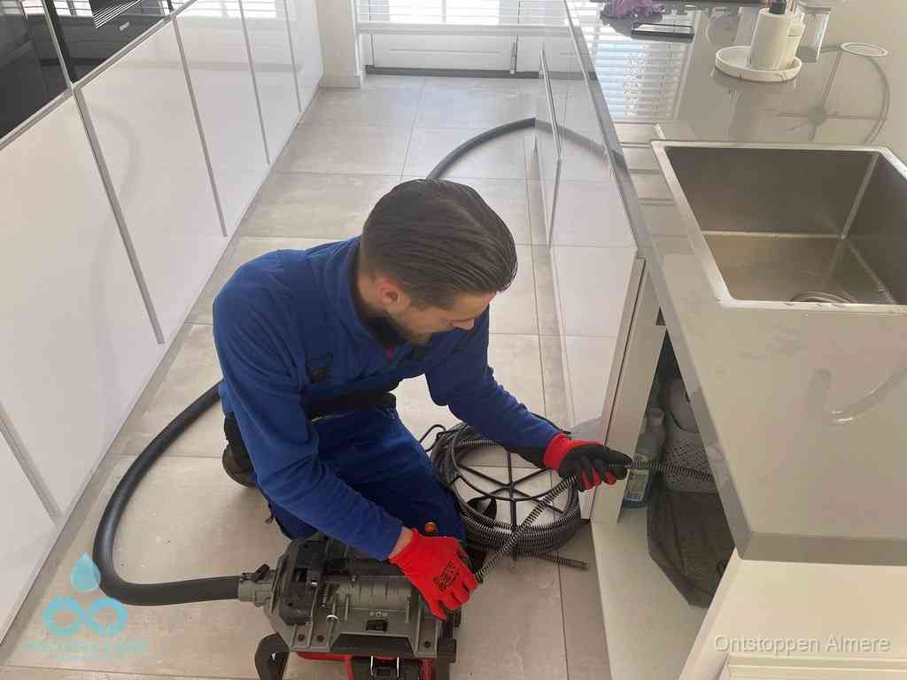 Een monteur ontstopt de keukenafvoer onder de spoelbak met een elektrische veermachine in Almere