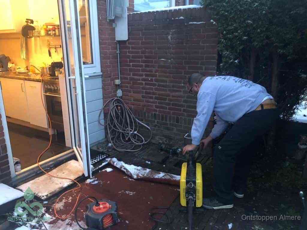 Een monteur werkt buiten bij een open riool-/grondput met een elektrische ontstoppingsmachine om een verborgen afvoerprobleem op te sporen in Almere