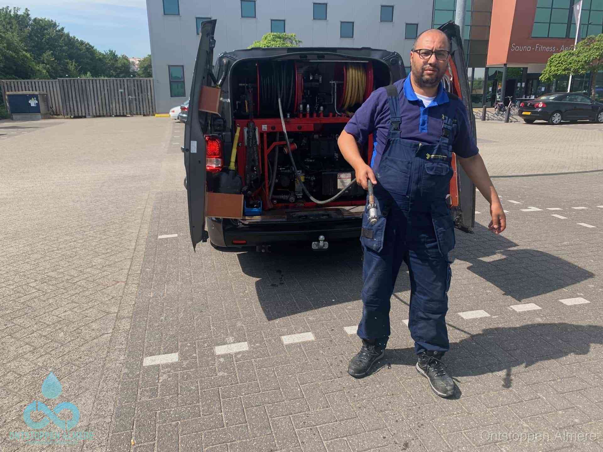 Een monteur bij zijn bestelbus met een hogedruk- en rioolreinigingsunit, klaar om de oorzaak van terugkerende wc-verstoppingen aan te pakken in Almere