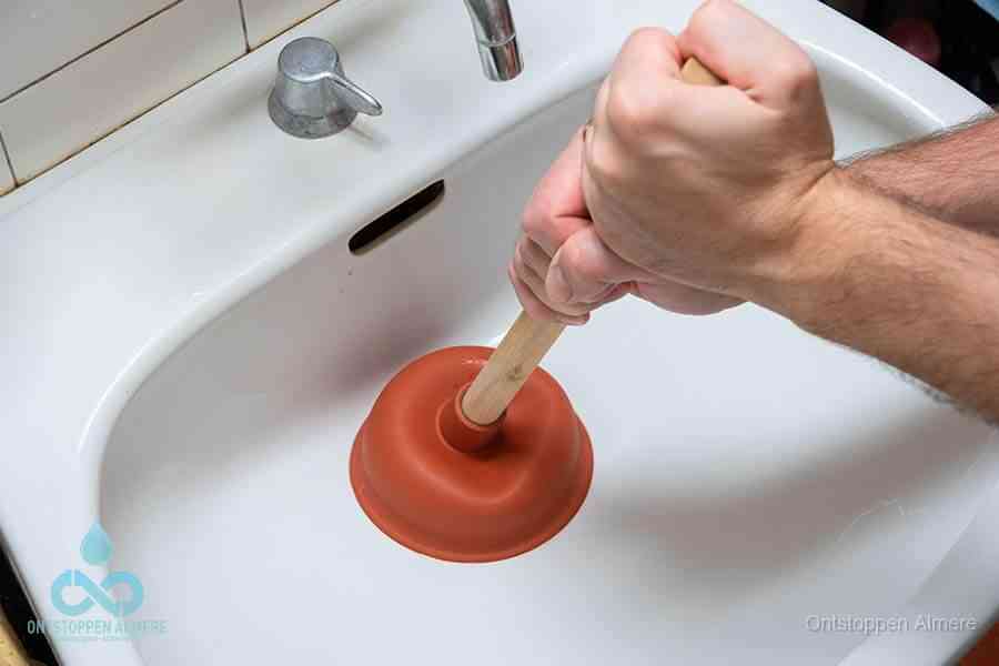 Twee handen gebruiken een rode rubberen plopper op een sanitair-afvoer om het toilet te ontstoppen in Almere