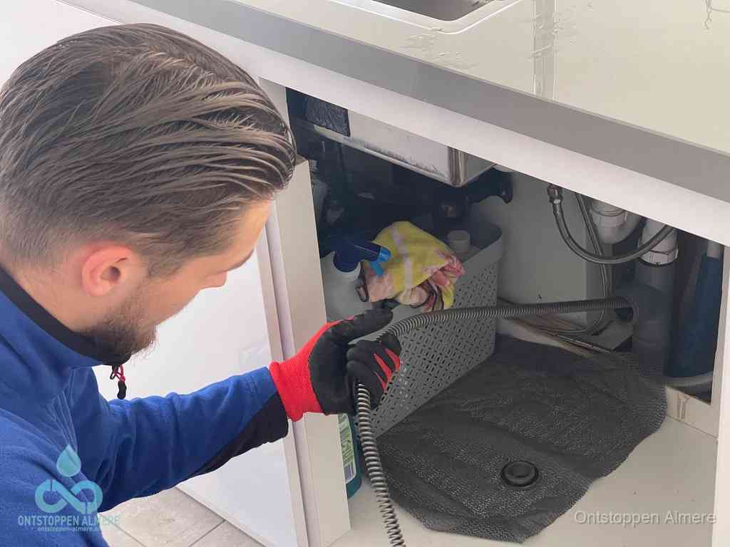 Een monteur voert een flexibele ontstoppingsveer in de afvoer om een verstopping voorbij de bocht van het toilet te bereiken in Almere