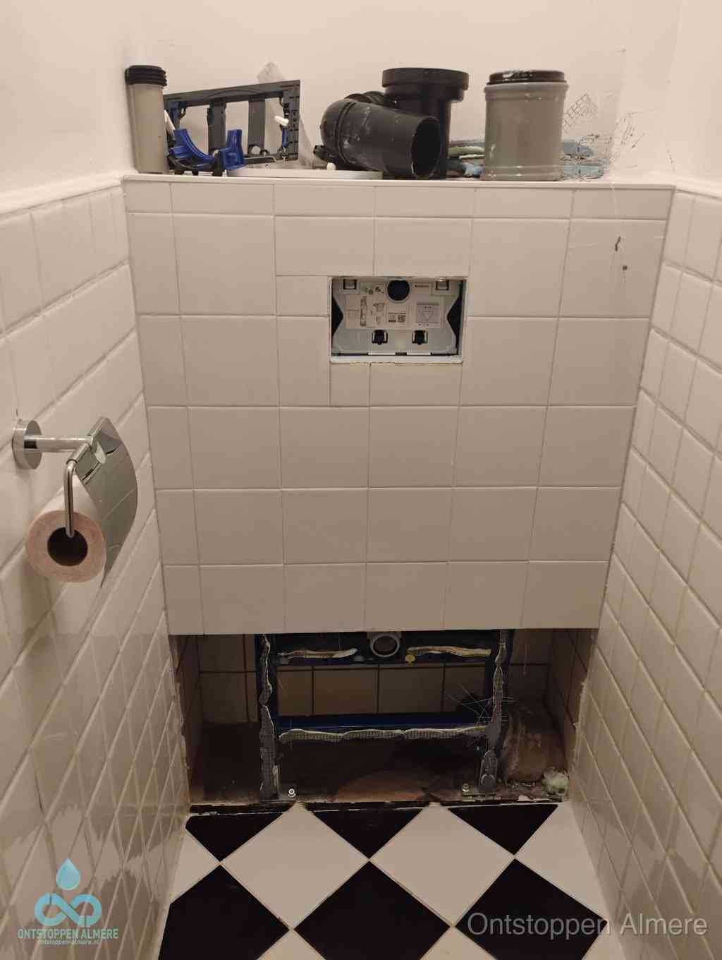 Een toiletruimte waar het hangtoilet en de inbouwreservoir-onderdelen zijn vrijgelegd voor onderhoud, periodiek nazicht voorkomt een wc-verstopping in Almere
