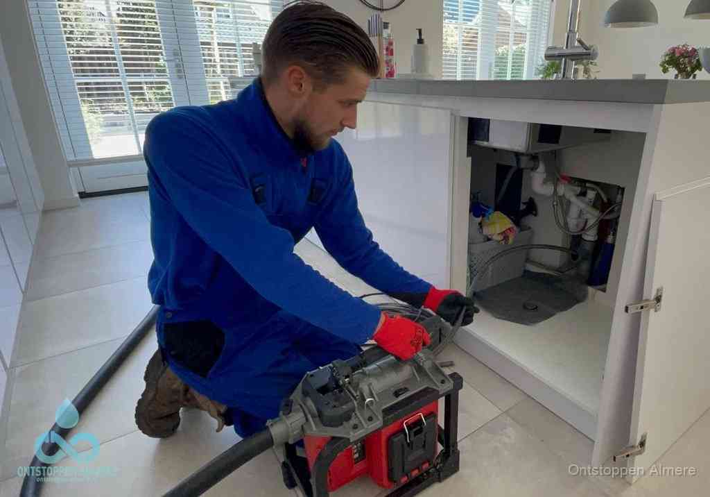 Een monteur voert een professionele elektrische ontstoppingsmachine in de afvoer onder de spoelbak tijdens het gootsteen ontstoppen in Almere