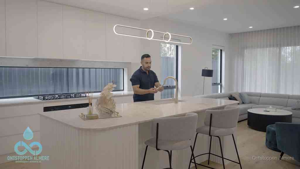 Een bewoner bij de keukenspoelbak die zelf aan de slag gaat met een verstopte gootsteen in Almere