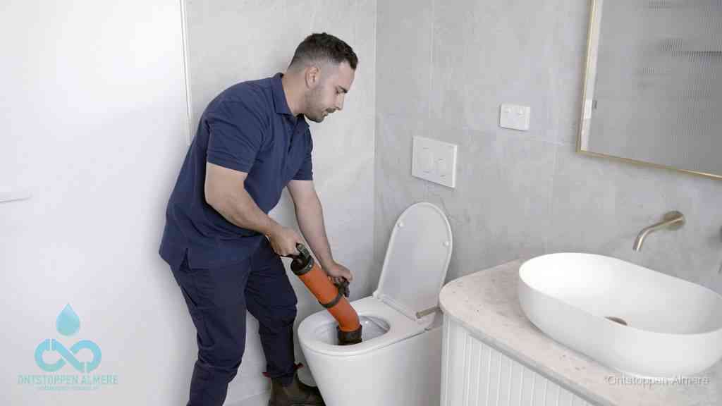 Een man gebruikt een handmatige luchtdruk-ontstopper in een modern betegeld toilet om zelf de wc te ontstoppen in Almere